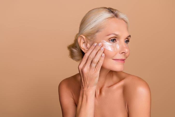Photo portrait of elderly lady putting on facial cream.